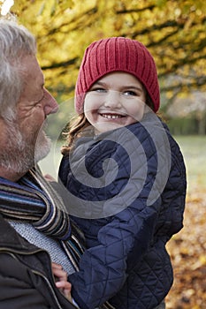 Grandfather Cuddling Granddaughter On Autumn Walk