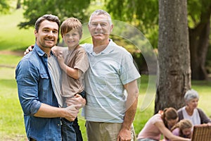 Grandfather father and son with family in background at park