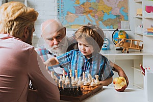 Grandfather father and son playing chess, happy men generations family. Granddad and cute little boy grandson study and