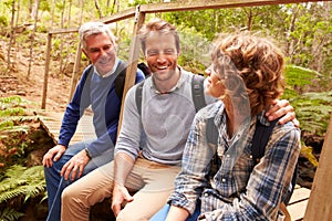 Grandfather, father and son sitting on a bridge in a forest