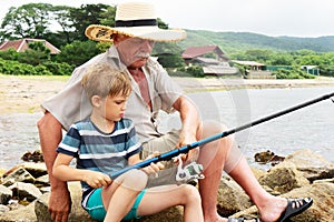Grandfather fisher in straw hat and little male grandkid enjoying leisure activity use fishing rod