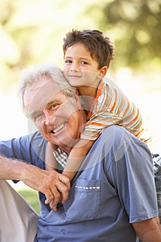 Grandfather Giving Grandson Ride On Back In Park