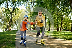 Grandfather giving roller skating class for little boy in park