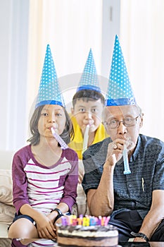 Grandfather and grandchildren blowing horns and wearing party hat