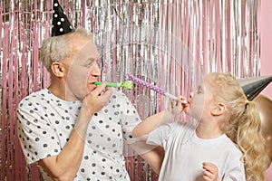 grandfather and granddaughter in caps have fun and blow a horn, hug and kiss on the eve of the holiday