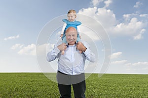 Grandfather with granddaughter on his shoulders, walking in mead