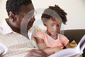 Grandfather And Granddaughter Reading Book At Home Together