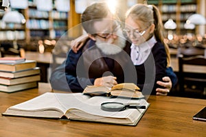 Grandfather and granddaughter reading a book in old vintage city library. Family reading, leisure, education concept