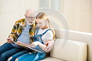 Grandfather and granddaughter reading book together at home