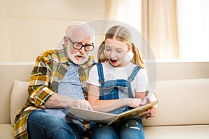 Grandfather and granddaughter reading book together at home