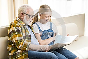 Grandfather and granddaughter reading book together at home