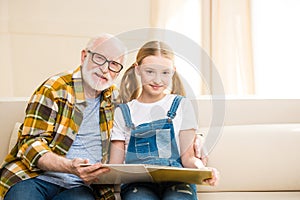 Grandfather and granddaughter reading book together at home