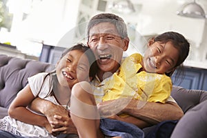 Grandfather And Granddaughters Relaxing On Sofa At Home