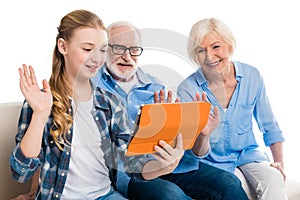 Grandfather, grandmother and grandchild using digital tablet and sitting on sofa