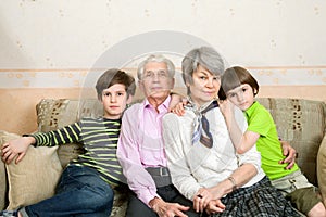 Grandfather, grandmother and grandchildren are sitting on sofa