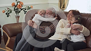 Grandfather and grandmother sitting on leather sofa in modern living room with two small girls near. Granddaughters