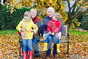 Grandfather, grandmother and two little kid boys, grandchildren sitting in autumn park.