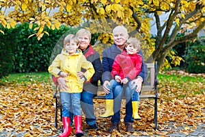 Grandfather, grandmother and two little kid boys, grandchildren sitting in autumn park.