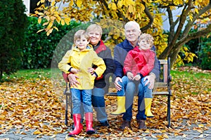 Grandfather, grandmother and two little kid boys, grandchildren sitting in autumn park.