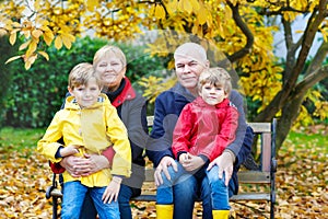 Grandfather, grandmother and two little kid boys, grandchildren sitting in autumn park.