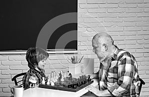 Grandfather and grandson boy playing chess, men generation. Different ages, grandfather and child grandson study chess