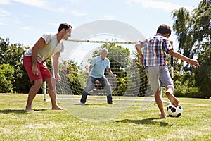 Grandfather, Grandson And Father Playing Football In Garden