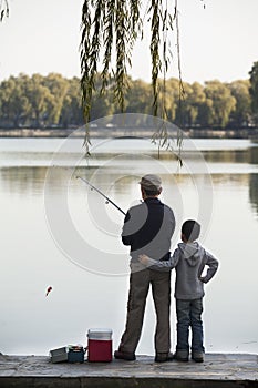 Grandfather and grandson fishing off of dock at lake