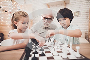 Grandfather, grandson and granddaughter at home. Children and grandpa are playing chess.