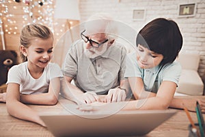 Grandfather, grandson and granddaughter at home. Grandpa and children are using laptop.