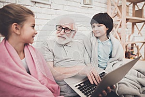 Grandfather, grandson and granddaughter at home. Grandpa and children are watching movie on laptop.