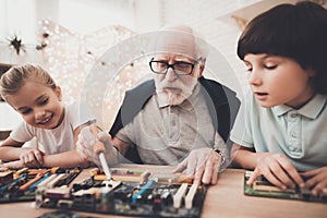 Grandfather, grandson and granddaughter at home. Grandpa teaches children how to braze.