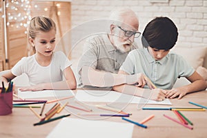 Grandfather, grandson and granddaughter at home. Children are drawing.