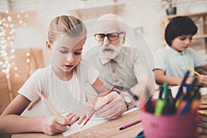 Grandfather, grandson and granddaughter at home. Children are drawing.