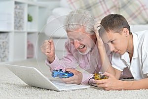 Grandfather and grandson lying on floor and playing computer games on laptop