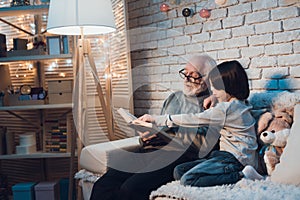 Grandfather and grandson at night at home. Granddad is reading fairy tales book.