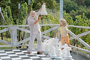 Grandfather and grandson playing chess on big chess board. Elderly old relative wit child.