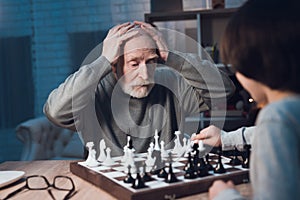 Grandfather and grandson are playing chess together at night at home.