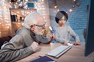 Grandfather and grandson are playing games on computer at night at home.