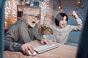 Grandfather and grandson are playing games on computer at night at home.