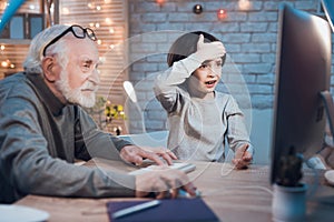 Grandfather and grandson are playing games on computer at night at home. Boy is cheering for granddad.