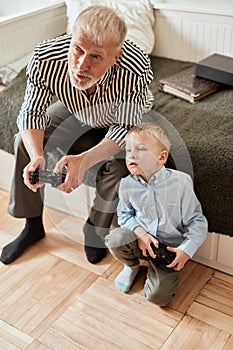 Grandfather and grandson playing video games on computer with joystick