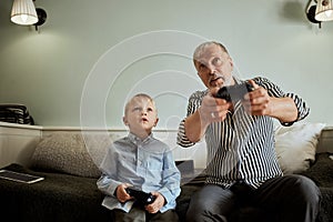 Grandfather and grandson playing video games on computer with joystick