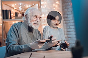 Grandfather and grandson are playing video games on computer at night at home.