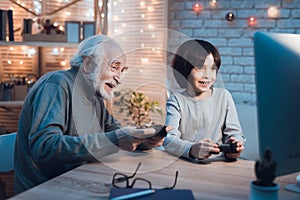 Grandfather and grandson are playing video games on computer at night at home.