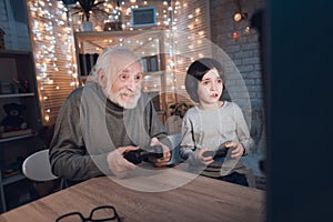 Grandfather and grandson are playing video games on computer at night at home.