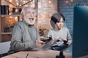 Grandfather and grandson are playing video games on computer at night at home.