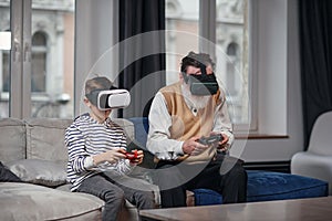 Grandfather and grandson are playing video games on computer at table at night at home.