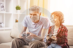 Grandfather and grandson are playing video games at home.