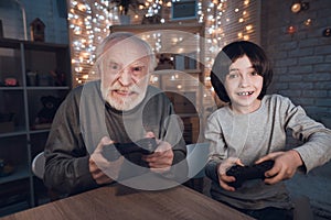 Grandfather and grandson are playing video games at night at home.