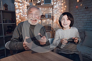 Grandfather and grandson are playing video games at night at home.